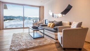 Un salon moderne comprenant un canapé, des fauteuils, une table basse et une grande fenêtre donnant sur des montagnes enneigées.