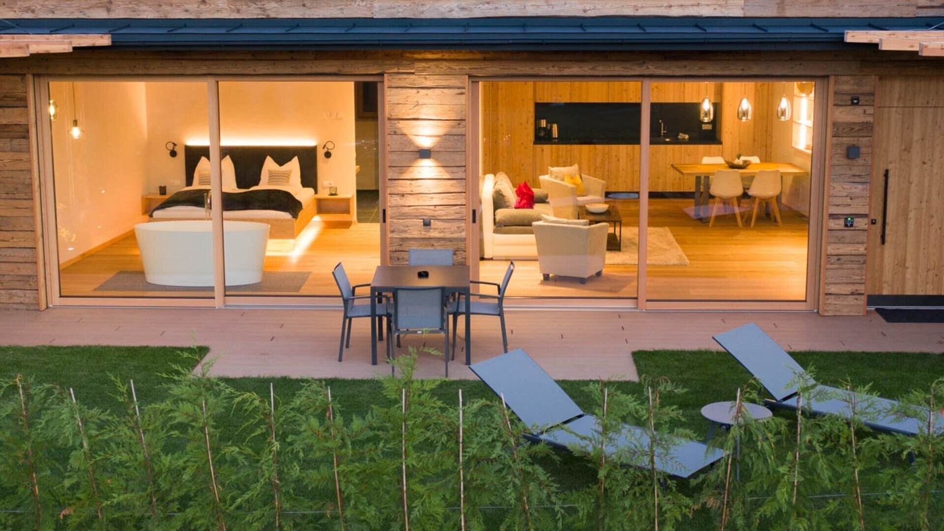 Ein modernes Haus mit einem verglasten Wohnbereich, einem Essbereich und einer Terrasse mit Liegestühlen.