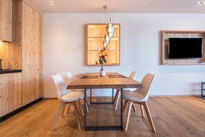 Zona pranzo moderna con tavolo in legno, sedie bianche, lampadario a sospensione e pensile in legno.