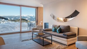 A modern living room with a large window, a sofa, a coffee table, and a unique wall mirror. - Beautiful Holiday Apartment "Aura Chalets No 4" with Mountain View, Wi-Fi & Garden (Kastelruth)