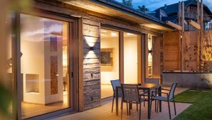 A modern house with a patio, sliding glass doors, and a wooden deck. - Beautiful Holiday Apartment "Aura Chalets No 4" with Mountain View, Wi-Fi & Garden (Kastelruth)