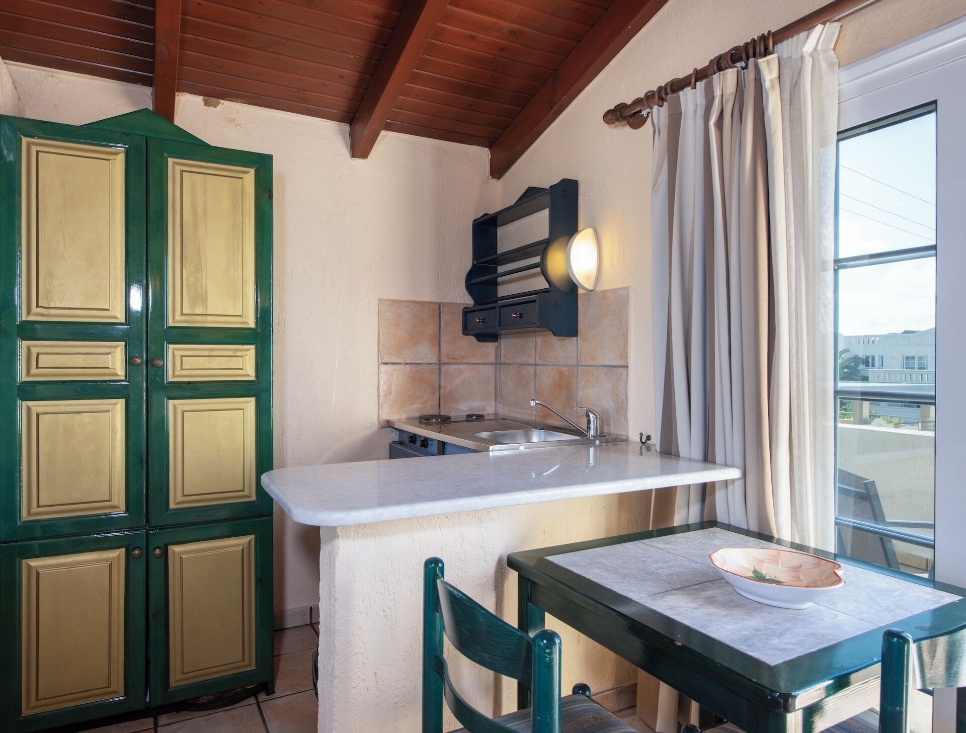 A compact kitchen with a built-in stove, a sink, and a window with curtains.