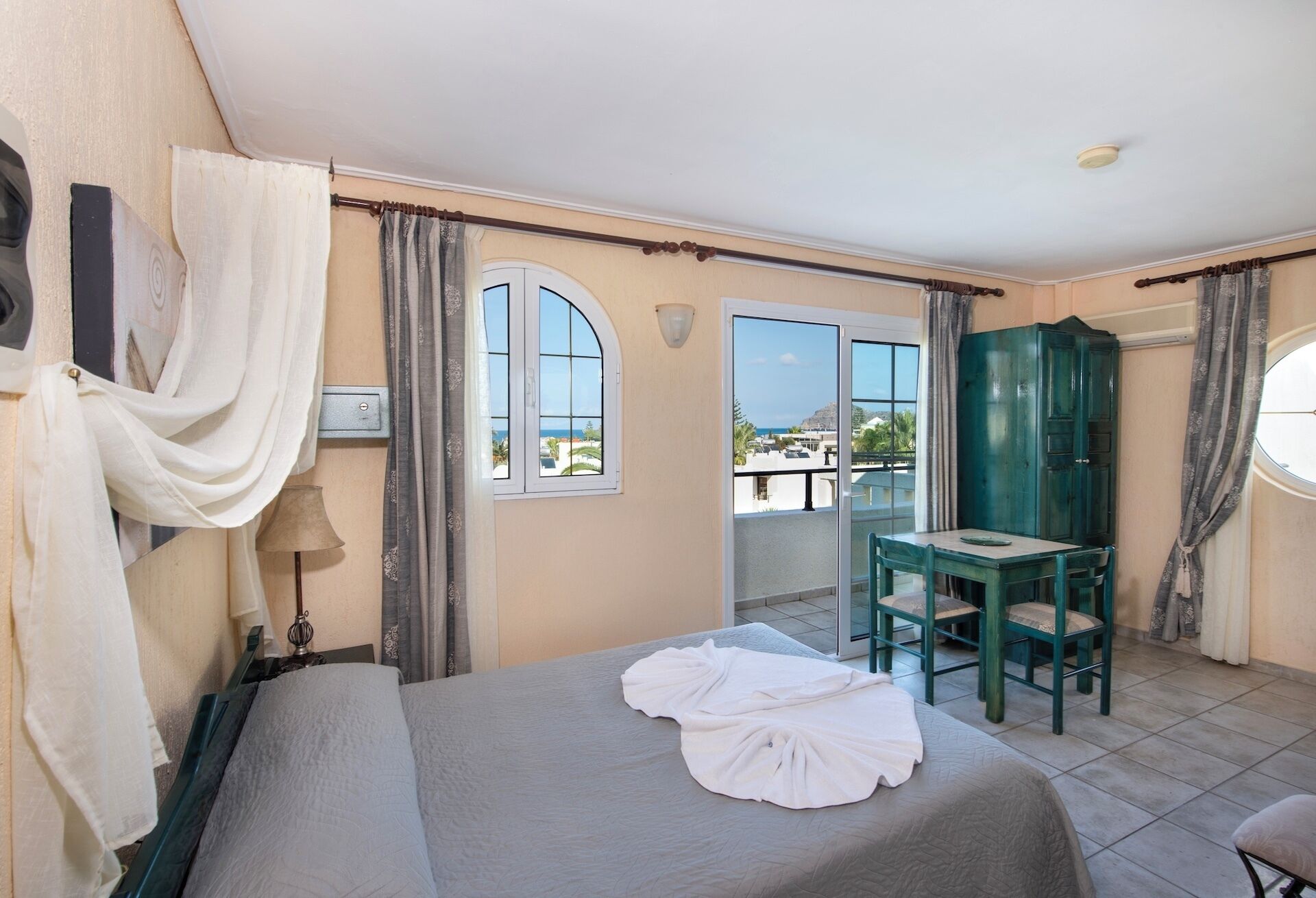 Une chambre d’hôtel avec un lit, une table et des chaises, une vue sur la mer et un meuble vert.