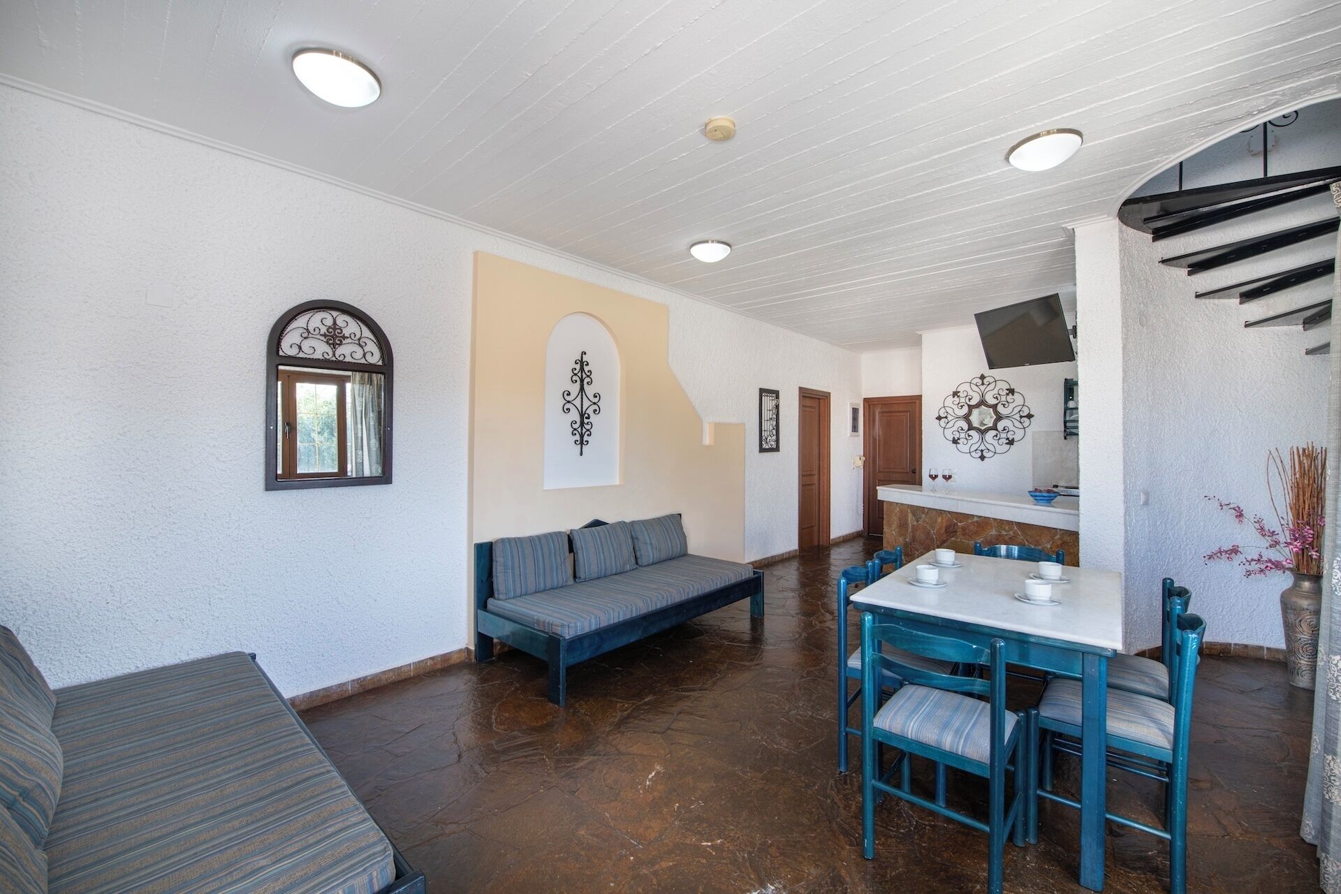 A dining area with a table and chairs, a sofa, and a kitchen area with a TV.