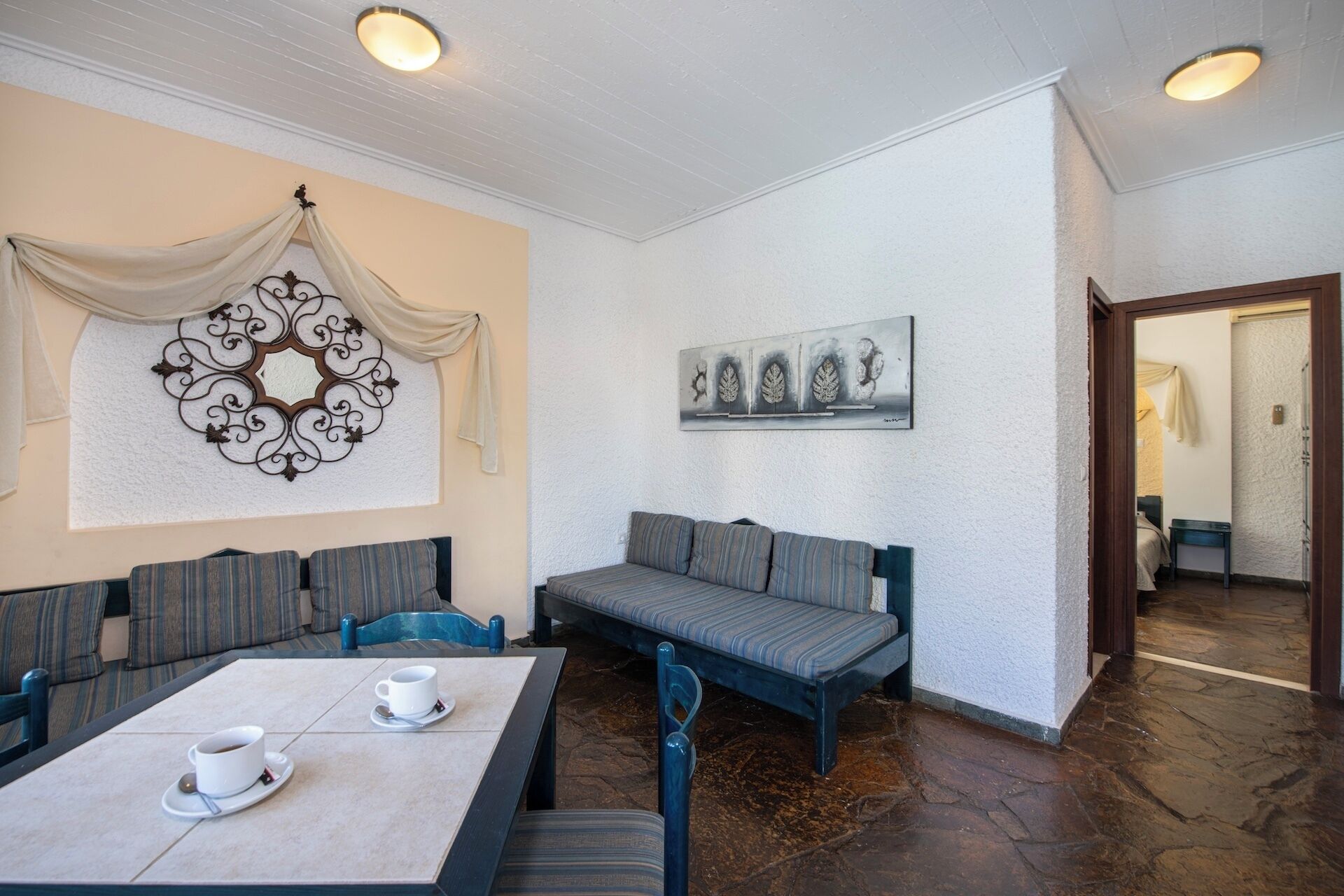 Un comedor con una mesa larga, sillas y un sofá. Se observan dos obras de arte colgadas en la pared y una pieza decorativa de metal.