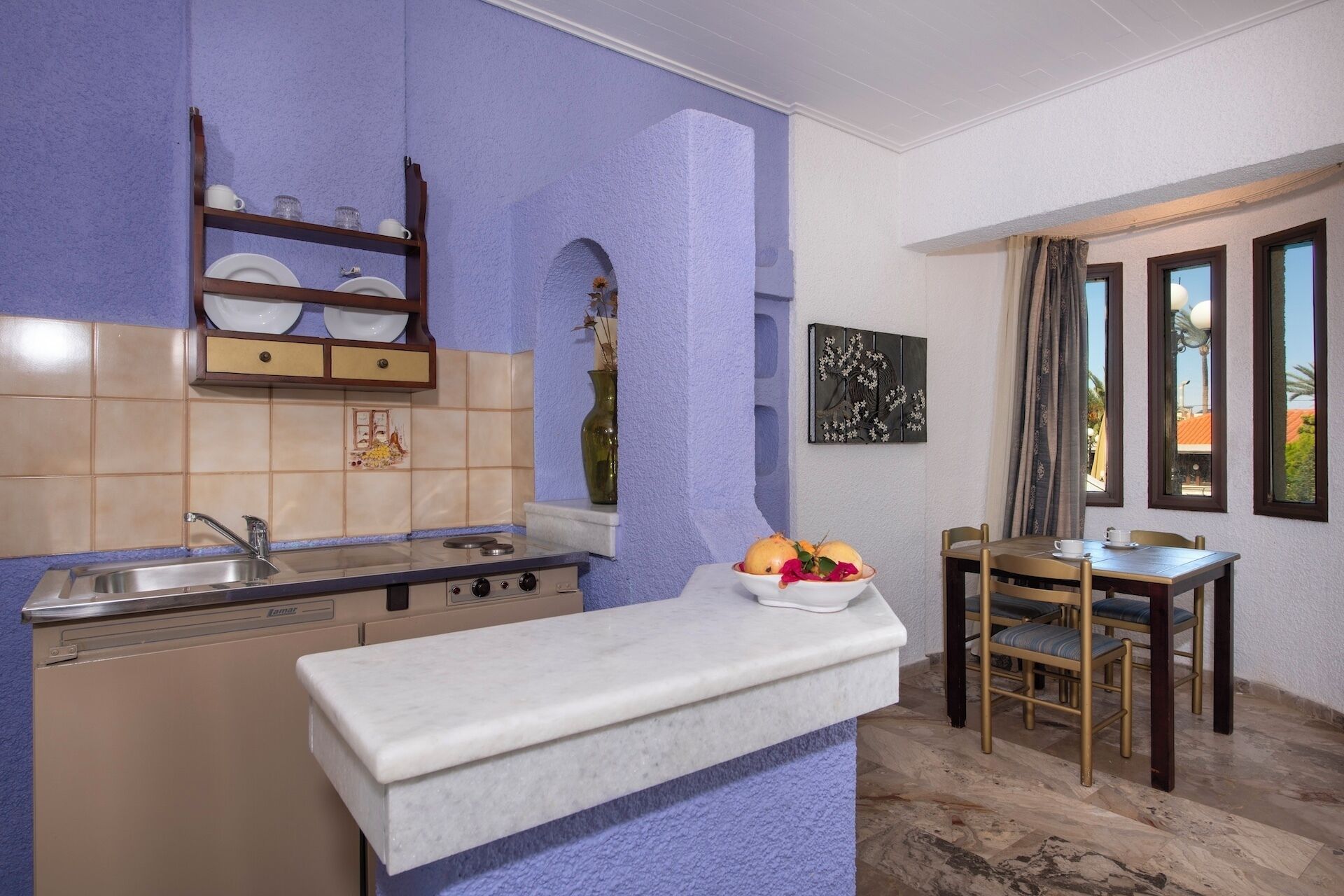 Cocina compacta con lavabo, estufa y un pequeño comedor con mesa y sillas.