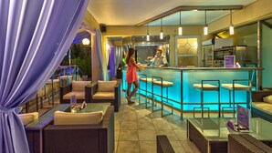 A bar area with a counter, bar stools, and a seating area with sofas and tables. - Hotel Castle Suites (Platanias)