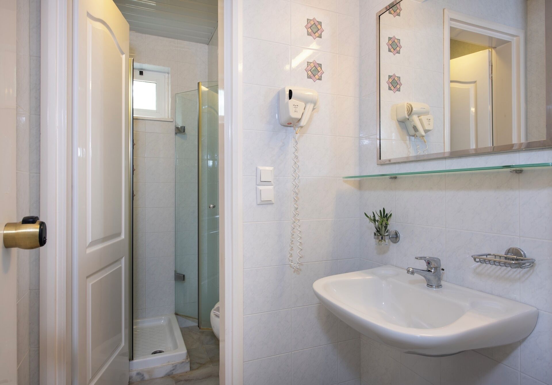 Un baño con cabina de ducha de vidrio, un lavamanos blanco con un solo grifo, un espejo sobre el lavamanos y un secador de pelo montado en la pared.