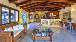 A spacious lobby with a high wooden ceiling, a reception desk, and a seating area with wicker furniture. - Hotel Castle Suites (Platanias)
