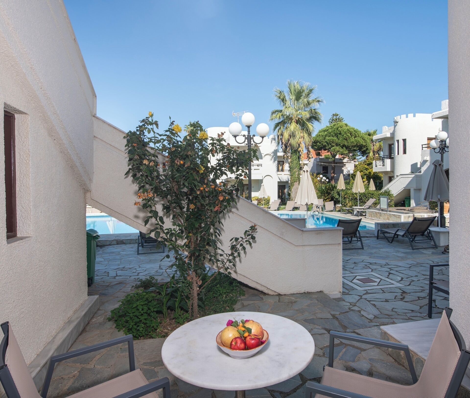 A courtyard with a pool, outdoor seating, and a small table with fruit.