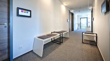 En hall med en bänk, ett litet bord och en digital skärm på väggen.