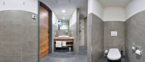 Un baño moderno con puerta de madera, lavabo con espejo, zona de ducha e inodoro.