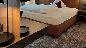 Una habitación de hotel moderna con una cama grande, un cabecero con diseño de rombos, lámparas de noche y una alfombra estampada.
