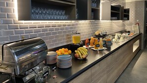 Una barra de desayuno moderna con máquina de café, fruta y dispensadores de zumo.