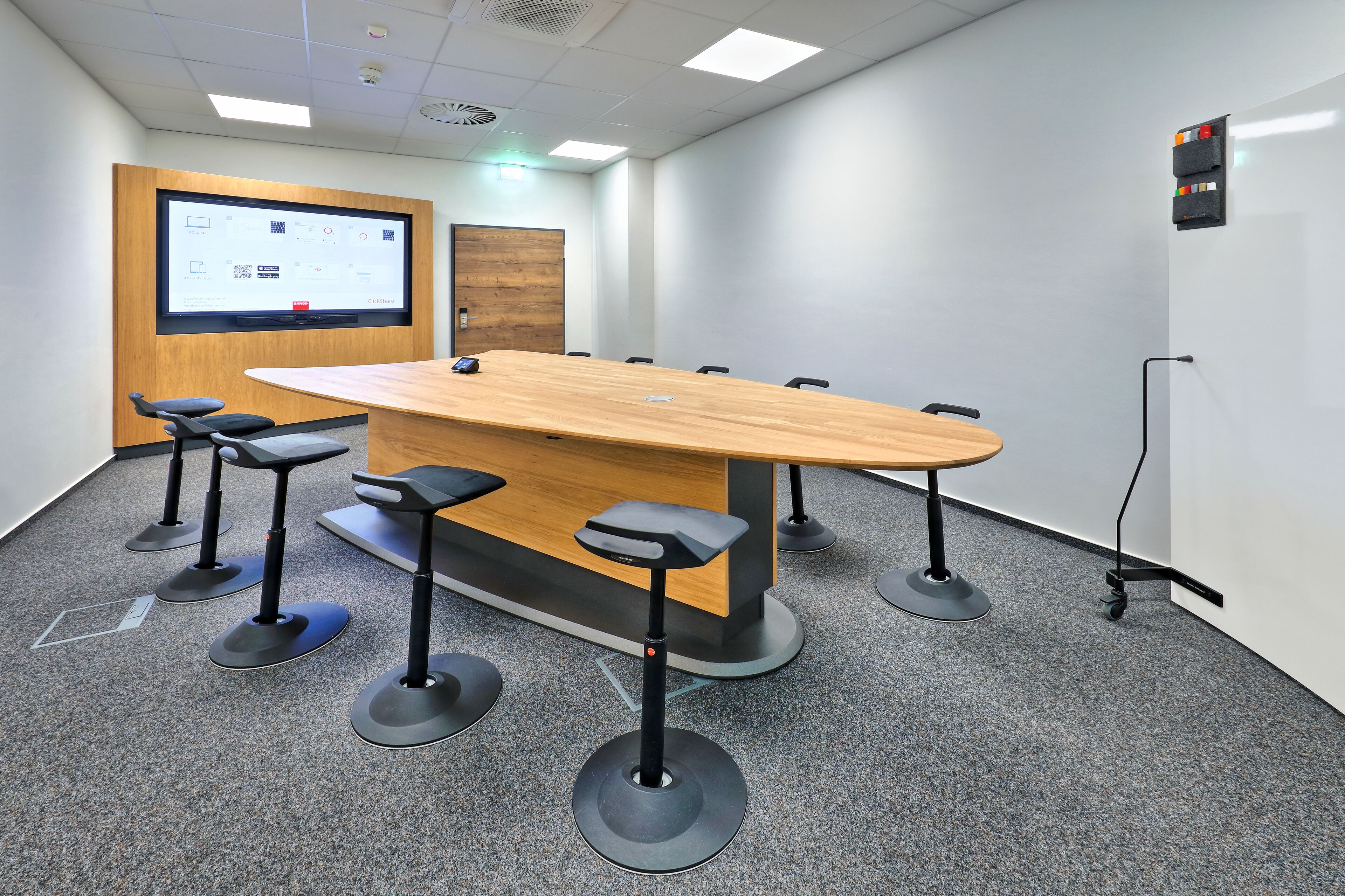A conference room with a long table, four bar stools, a projector screen, and a whiteboard.