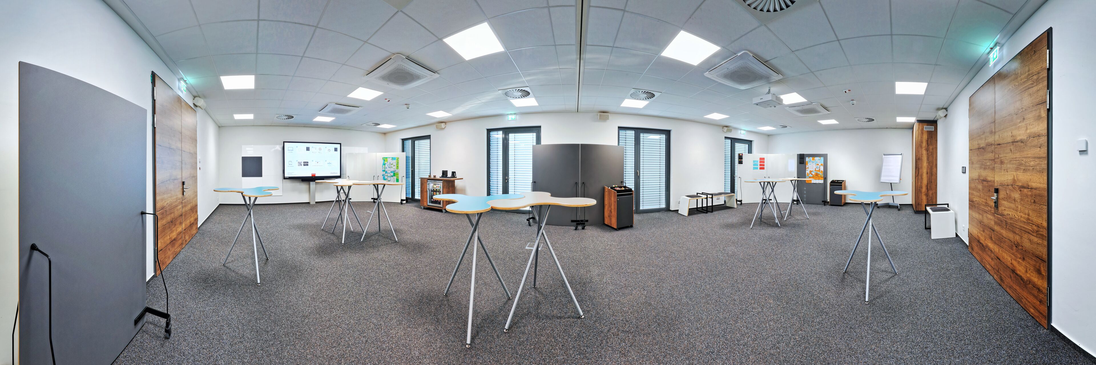 Une salle de conférence équipée d’un grand écran, de plusieurs tables et d’un tableau blanc.