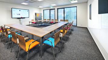 A conference room with a long table, multiple chairs, a projector screen, and a large window with blinds.