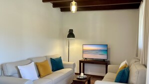 Een moderne woonkamer met een bank, fauteuils, een televisie, een lamp en een tafel met een kaars.