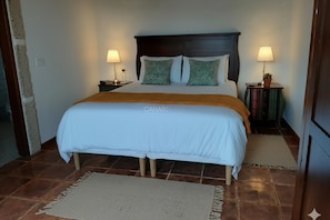 A bed with a white bedspread and two pillows, a wooden headboard, two bedside tables with lamps, and a rug on the floor.