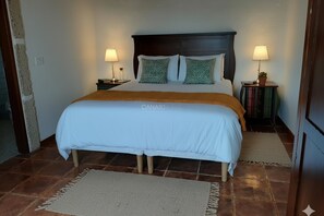 Una cama con colcha blanca y dos almohadas, cabecera de madera, dos mesitas de noche con lámparas y una alfombra en el suelo.
