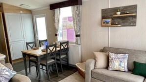 A living room with a sofa, a dining table with chairs, and a kitchen area with cabinets. - The Lizard Bluewater (Helston)