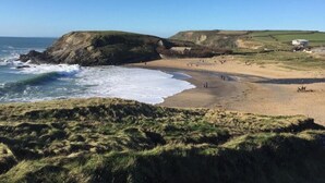 A coastal landscape with a sandy beach, grassy cliffs, and a clear blue sky. - The Lizard Bluewater (Helston)