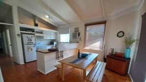 A compact kitchen with a central island, a dining table with benches, and a wooden floor.