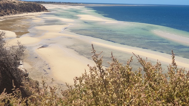 A coastal landscape with a sandy beach and clear blue waters.
