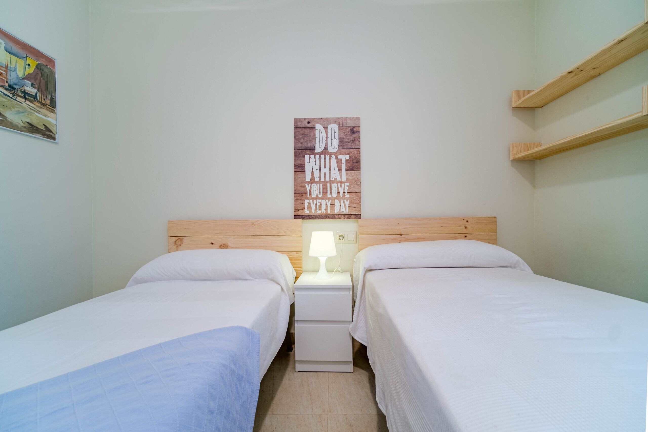 A bedroom with two single beds, a wooden headboard, a bedside table with a lamp, and a motivational poster on the wall.