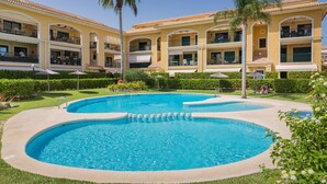 A hotel with a large outdoor swimming pool, multiple balconies, and lush landscaping.