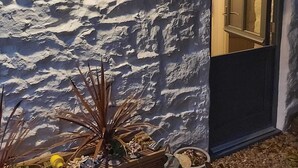A rustic stone wall with a wooden planter box containing plants and decorative items. - Detached comfortable granite cottage, 5 minute walk to the beach - Dogs Welcome (Penzance)