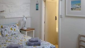 A bedroom with a bed, a desk, a chair, a hanging light fixture, and a door leading to another room. - Detached comfortable granite cottage, 5 minute walk to the beach - Dogs Welcome (Penzance)