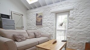A cozy living room with a sofa, a wooden coffee table, and a white textured wall. - Detached comfortable granite cottage, 5 minute walk to the beach - Dogs Welcome (Penzance)