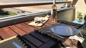 A balcony with a wooden table, a bottle of wine, a glass, a plate, and a dog. - NEW !! Full sea view. Charming apartment 3 bedrooms private parking  (Cabourg)