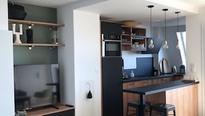 A modern kitchen with a central island, bar stools, and a dog bed. - NEW !! Full sea view. Charming apartment 3 bedrooms private parking  (Cabourg)