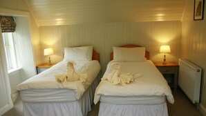 A room with two single beds, each with a nightstand and a lamp. The room has white walls and a sloped ceiling.