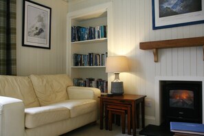 A living room with a sofa, a bookshelf, a lamp, a fireplace, and a television. - Traditional Cottage in the centre of Glencoe (Glencoe)
