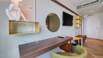 Ein modernes Hotelzimmer mit einem Holzbüro, einem grünen Sessel, einem großen Spiegel und einem flachbildfernseher an der Wand.