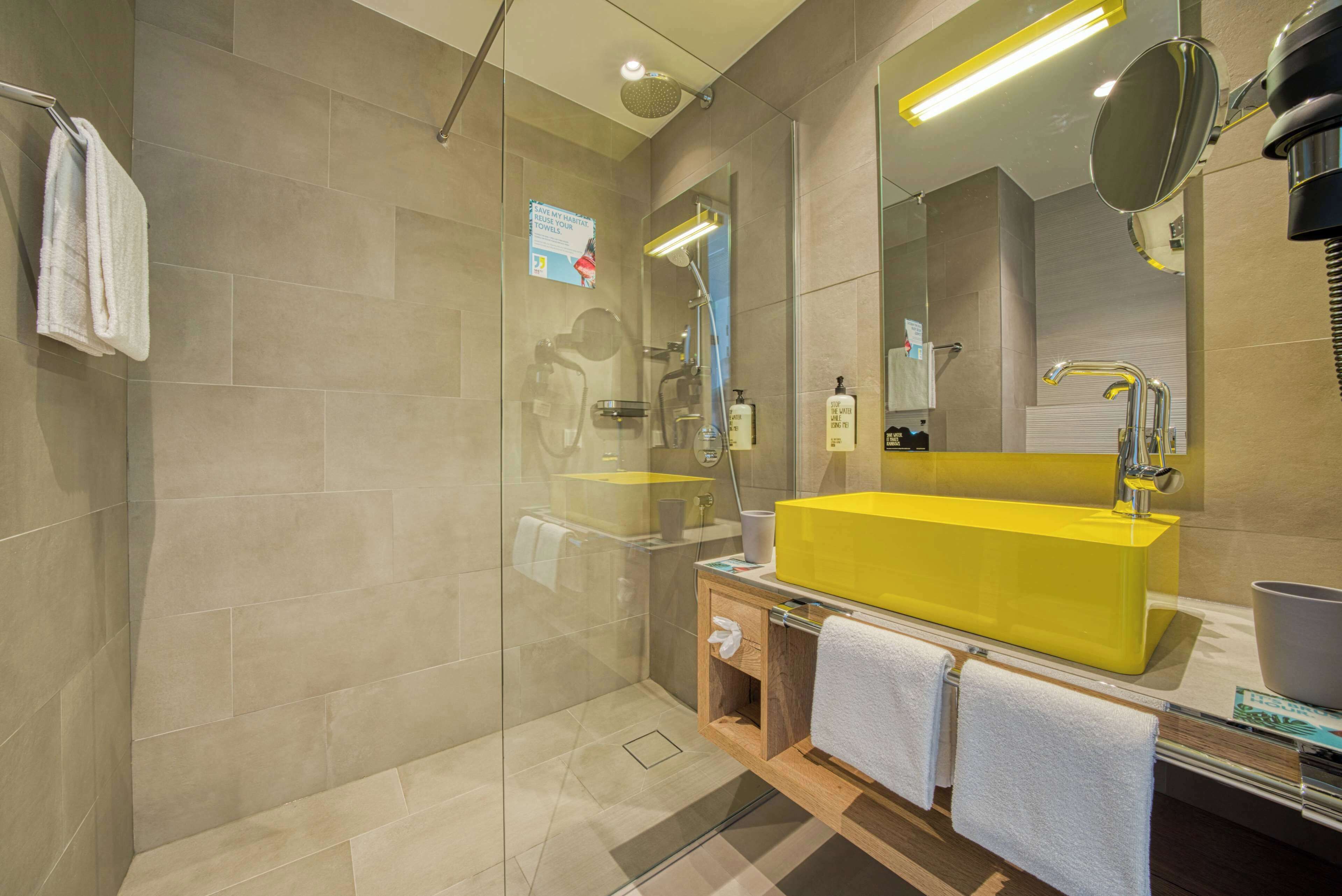 Une salle de bain moderne avec une douche à parois de verre, un lavabo jaune et un meuble-lavabo en bois.