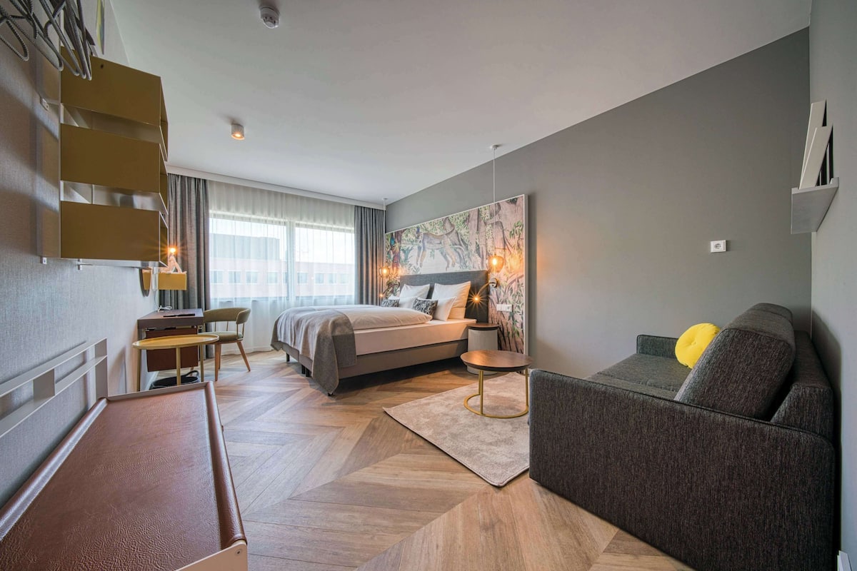 A modern hotel room with a bed, a sofa, a desk, and a billiards table.