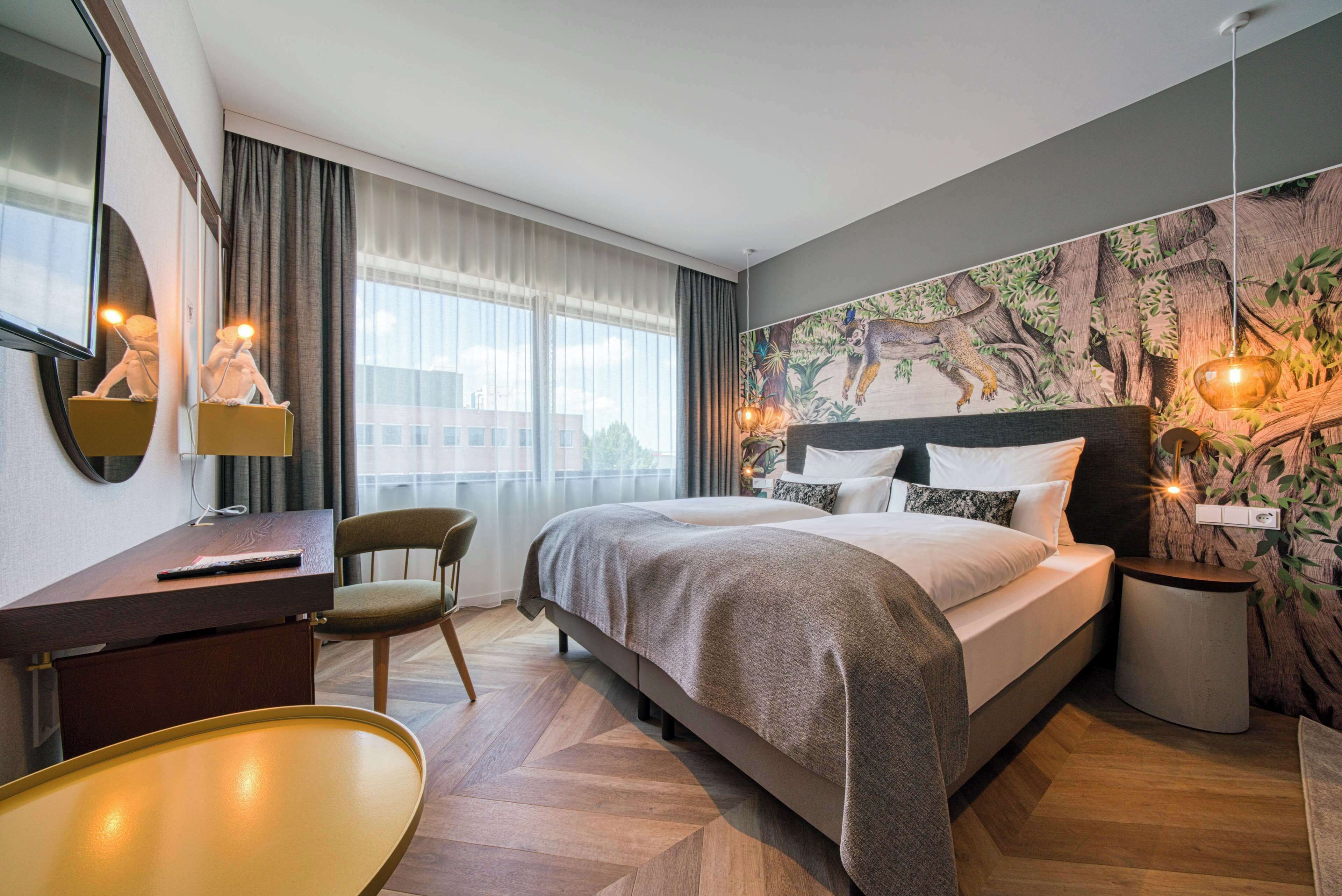 Et moderne hotelværelse med en stor seng, et skrivebord, en stol og et vægmaleri.