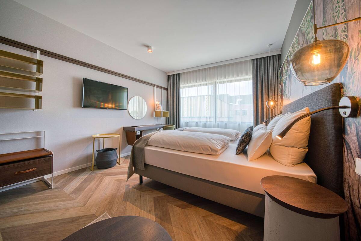 A modern hotel room with a bed, bedside table, lamp, and a television.
