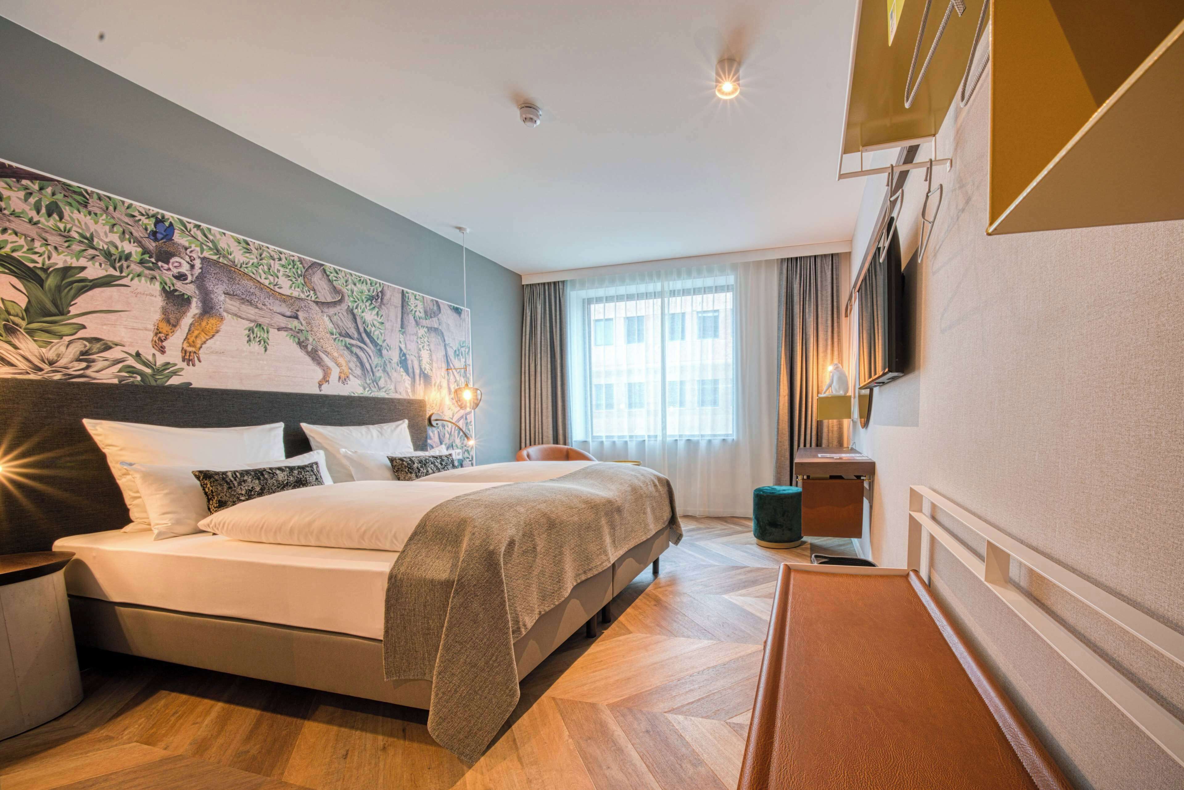 Une chambre d’hôtel avec un grand lit, une tête de lit ornée d’un tableau, un téléviseur à écran plat fixé au mur et une fenêtre avec des rideaux.