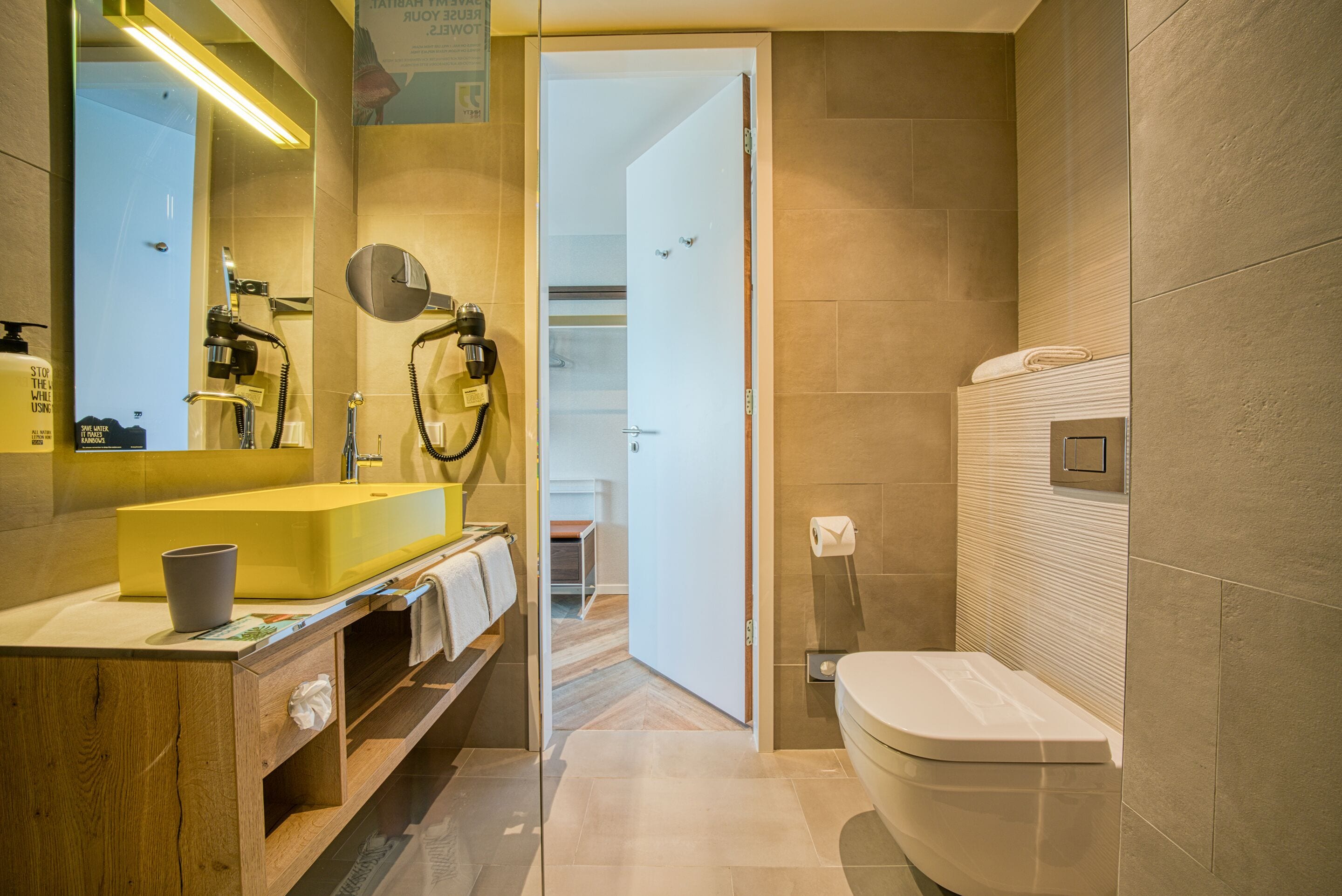 Un baño moderno con un lavabo amarillo, un espejo, un secador de pelo y un inodoro.