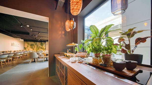 A modern cafe with a wooden counter, hanging pendant lights, and potted plants. - Vienna House Easy by Wyndham Amsterdam Airport (Hoofddorp)