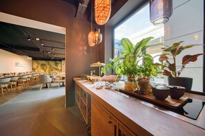 A modern cafe with a wooden counter, hanging pendant lights, and potted plants. - Vienna House Easy by Wyndham Amsterdam Airport (Hoofddorp)