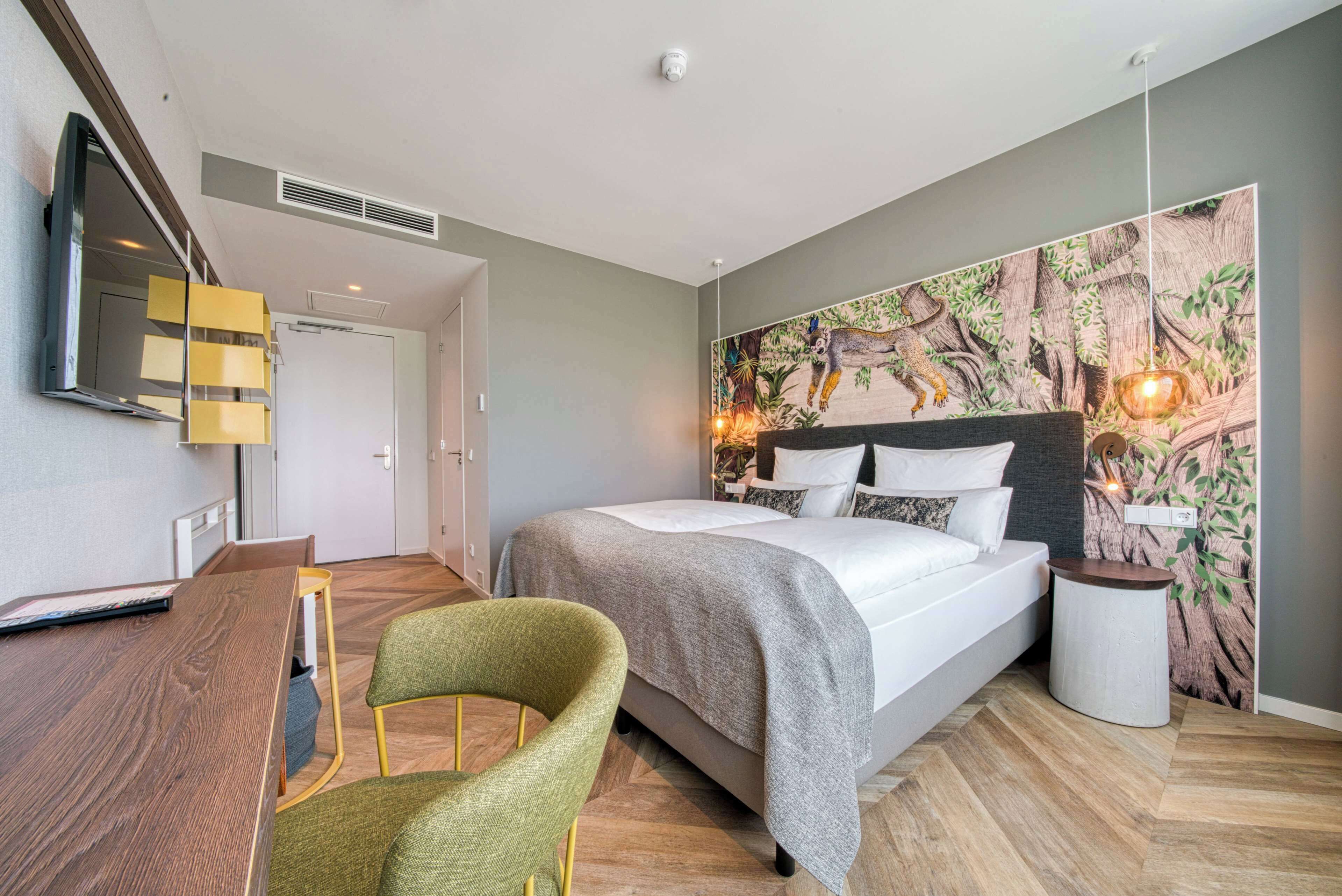 Een moderne hotelkamer met een bed, een bureau, een stoel en een groot wandtapijt.