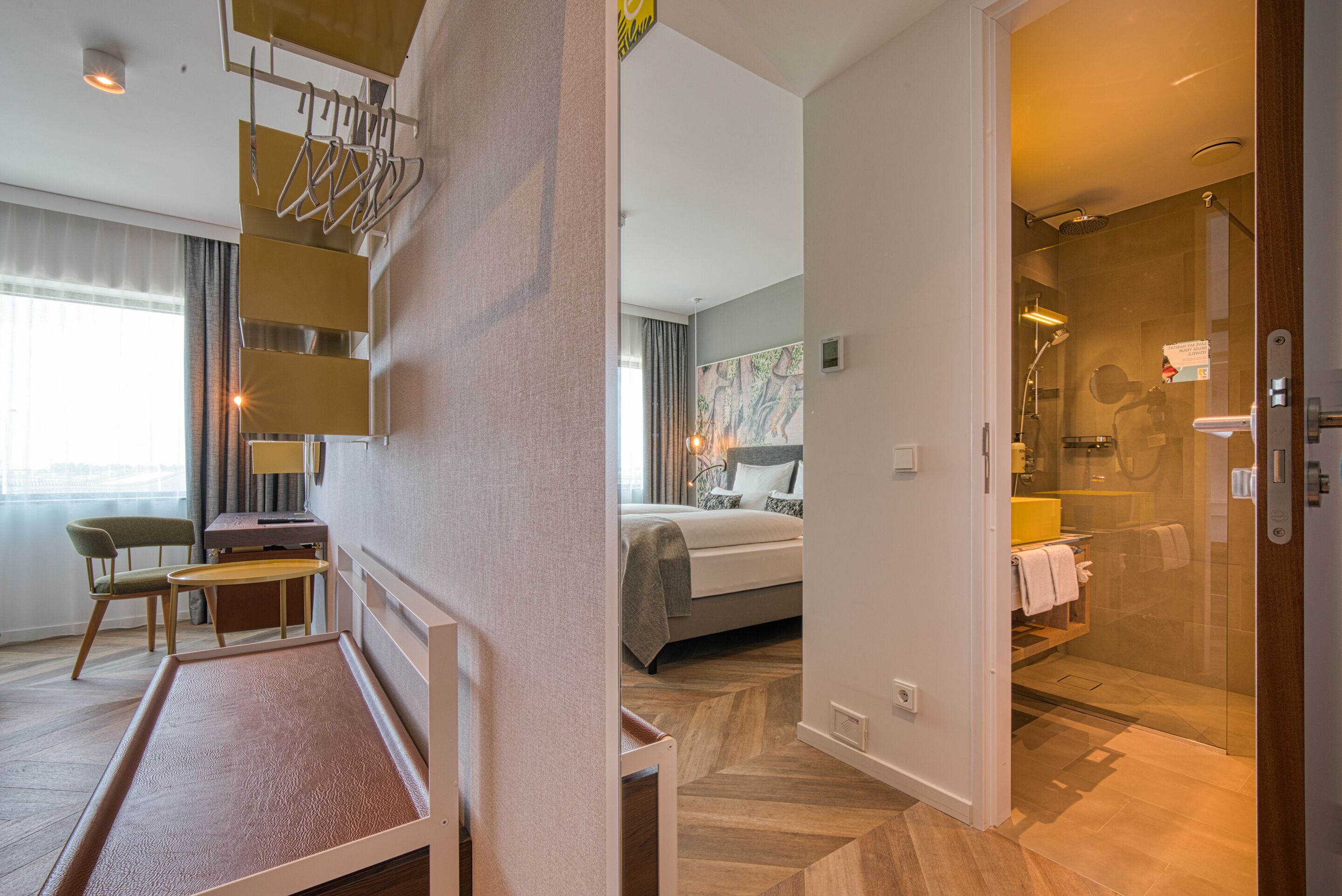 Ett hotellrum med en säng, ett skrivbord, en stol, en dusch och utsikt över staden.