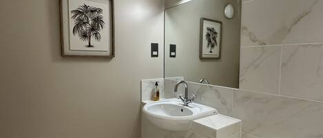 Un baño moderno con lavamanos de mármol, un espejo grande y obras de arte enmarcadas con palmeras.