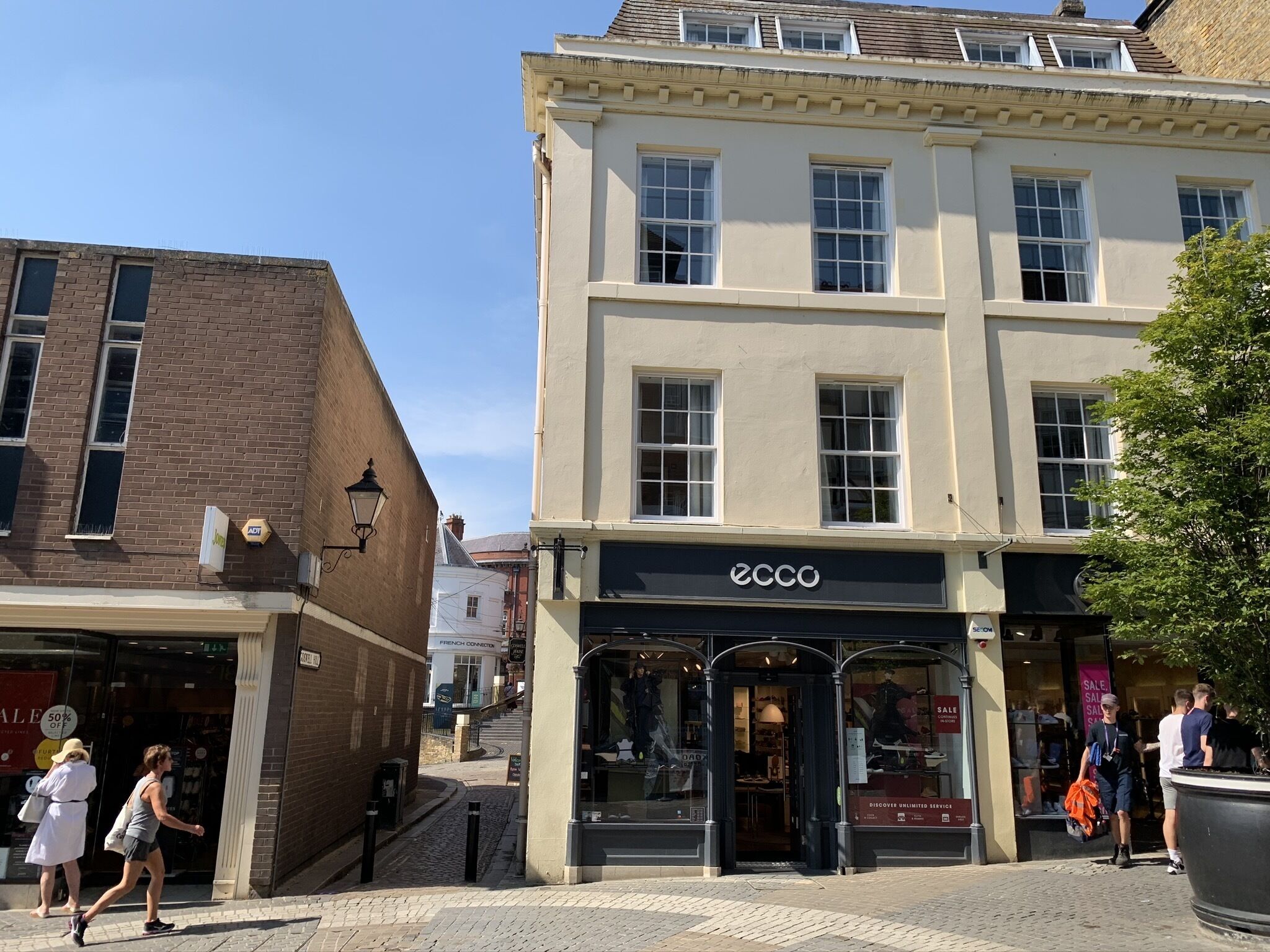 A street view with a building labeled 'ecco' featuring a storefront with mannequins and a sale sign.